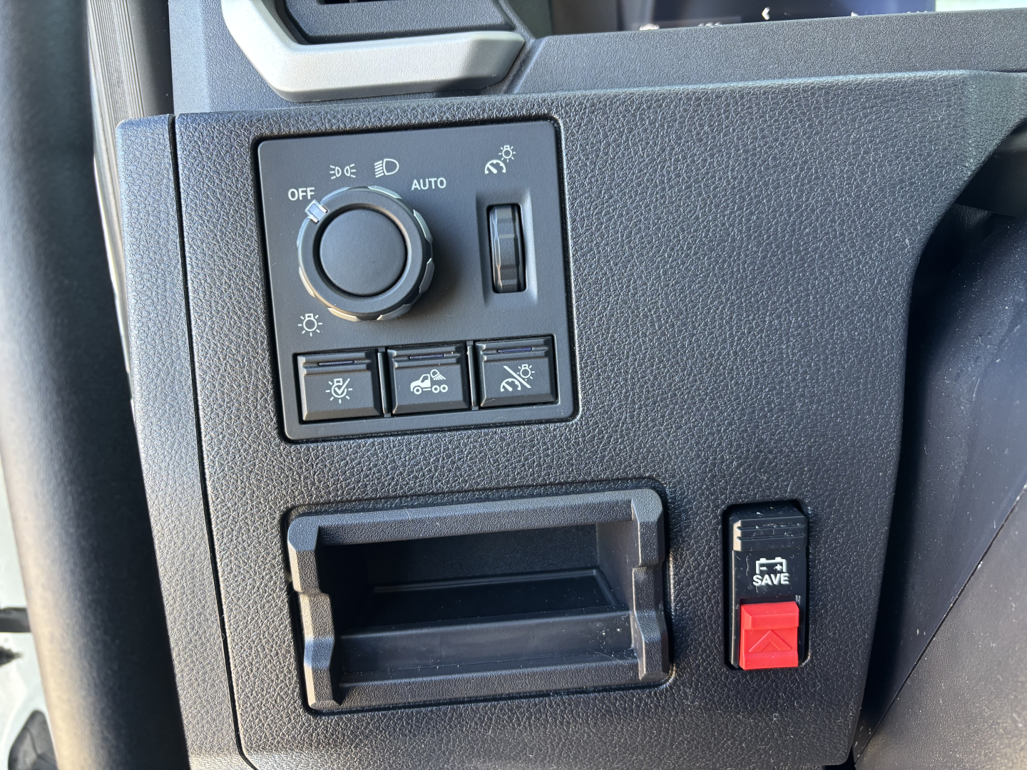 Dashboard panel with rotary headlight switch, several small buttons, a storage slot, and a red hazard/lock switch visible.