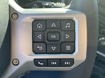 Steering wheel control panel with multiple buttons including home, up, down, OK, phone, and media controls visible on a Mack truck interior.