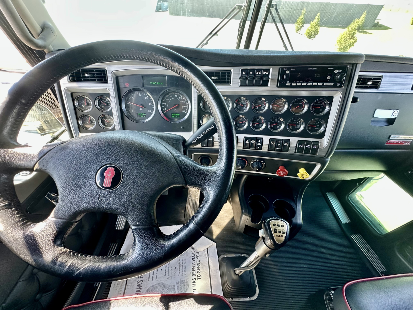 Kenworth W900L truck cab interior showing steering wheel, dashboard with multiple gauges and switches, gear shifter, and center console.