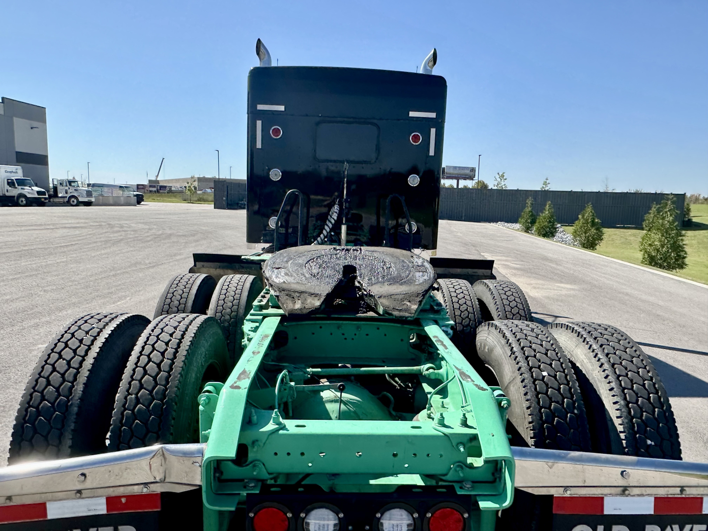 Kenworth W900L chassis rear view showing green frame, dual drive axles, and fifth wheel mounting with back of cab.