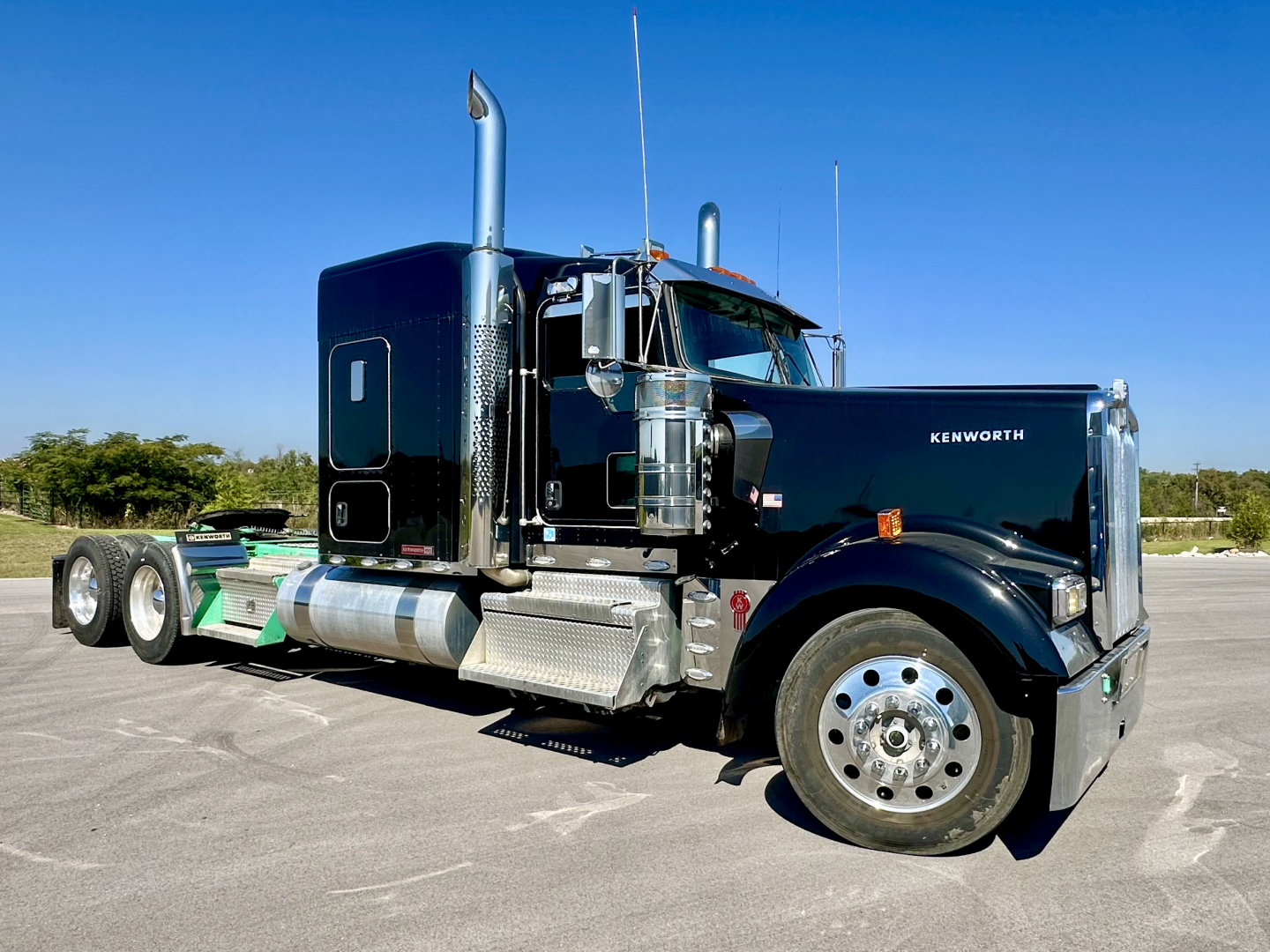 Kenworth W900L conventional sleeper truck in dark blue showing side exhaust stacks and chrome mirrors.