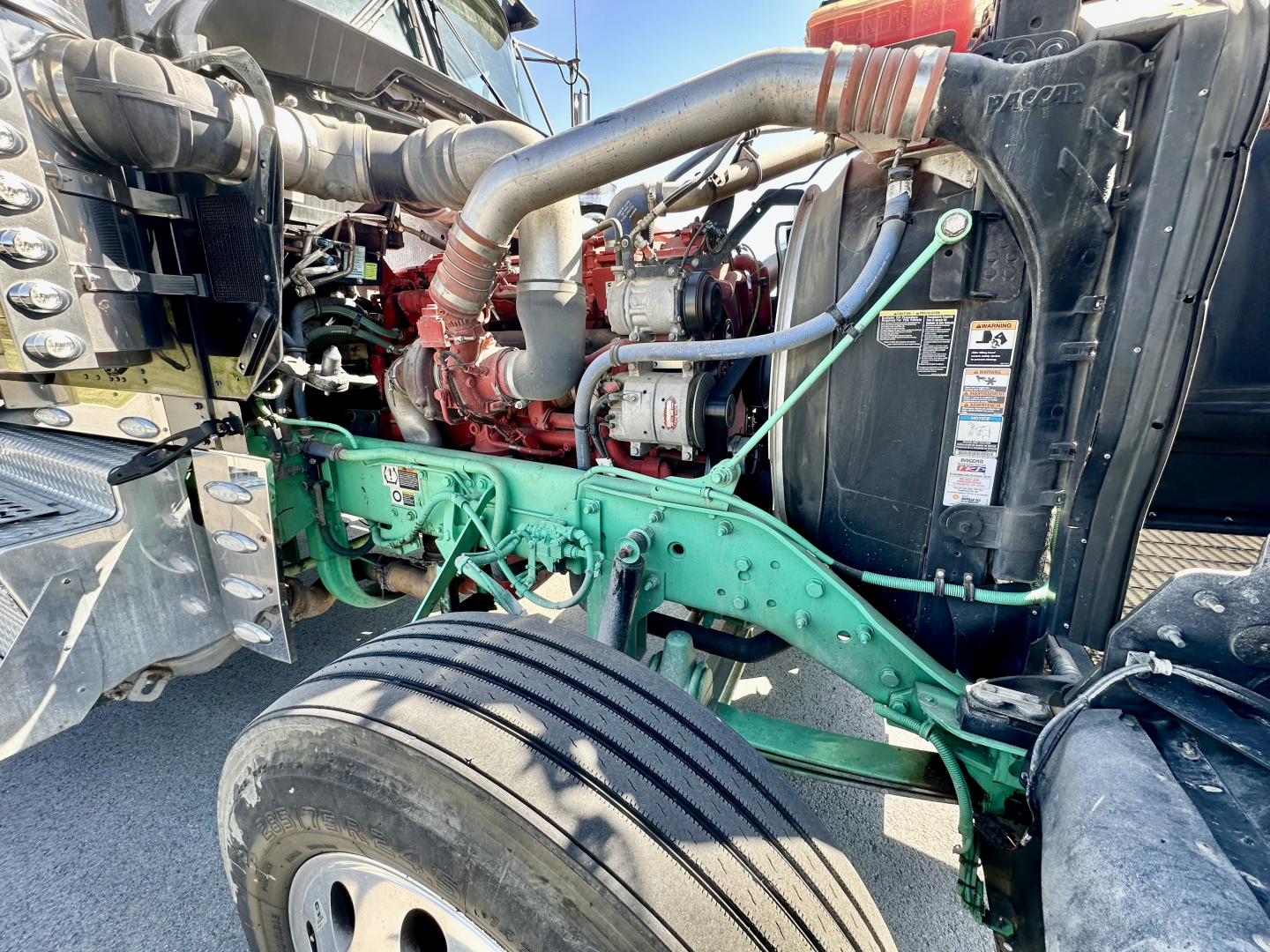 Kenworth W900L engine bay showing large turbocharger and coolant hoses with green frame and black radiator shroud.