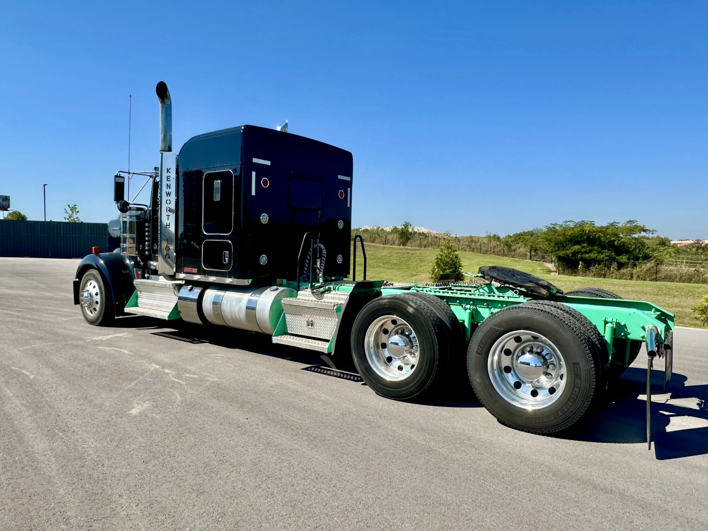 Kenworth W900L tractor in profile view showing chrome wheels and green chassis with sleeper cab, side exhaust, and dual rear axles.