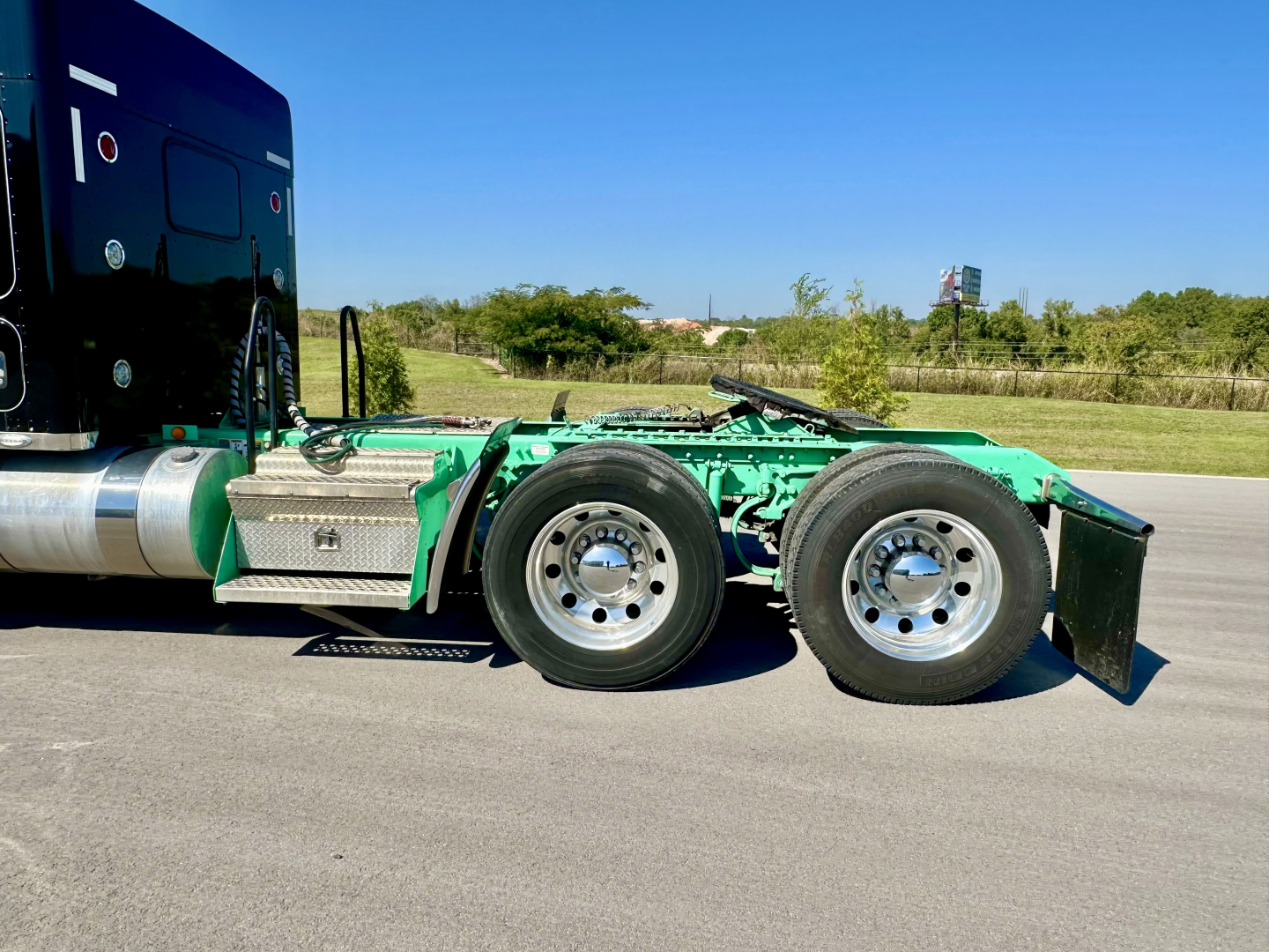 Kenworth W900L truck chassis side view showing green frame and dual rear wheels with aluminum fuel tank and side steps.