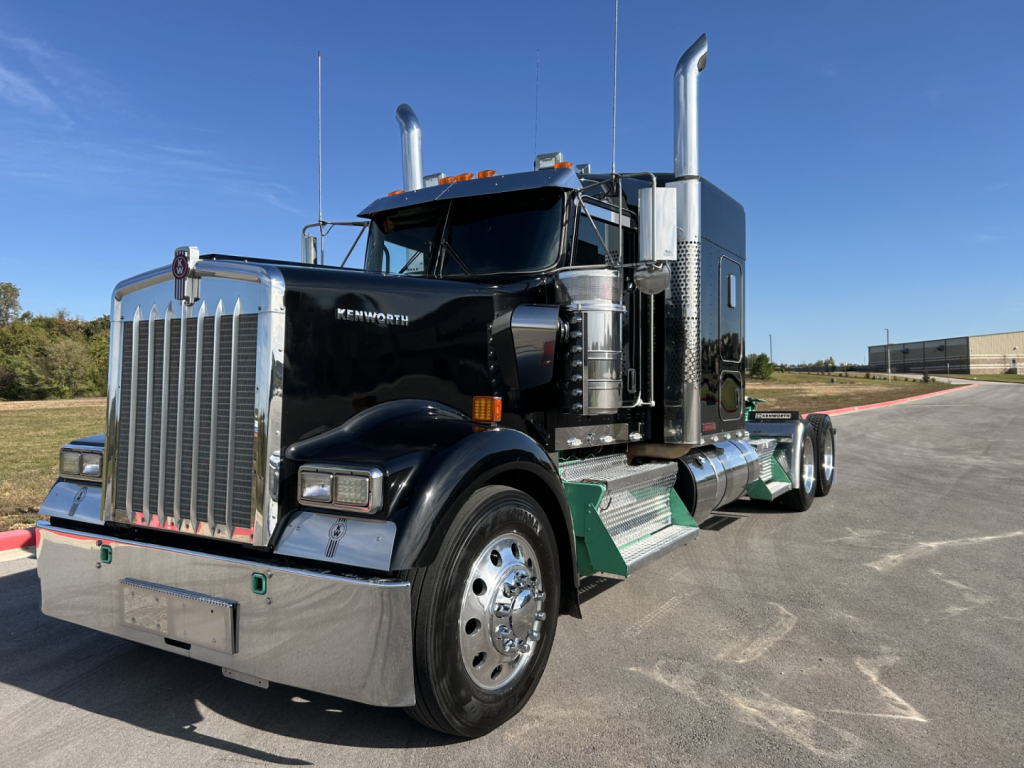 Kenworth W900L conventional sleeper truck in black with chrome exhaust stacks and polished bumper, front-left view.
