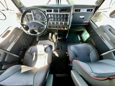 Kenworth W900L cab interior showing steering wheel, instrument cluster, dashboard controls, two seats, and center console.