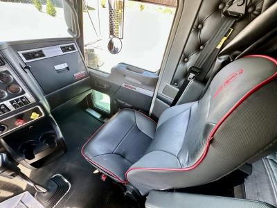 Kenworth W900L cab interior showing driver seat and dashboard with knobs and a silver panel; visible warning labels and control surfaces