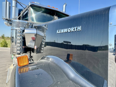 Kenworth W900L truck front fender and door with shiny black paint, Kenworth badge on the hood, large chrome side mirror, and orange turn signal light.