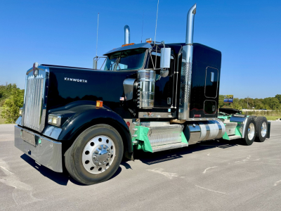 Kenworth W900L conventional sleeper truck in black, front-left view, chrome exhaust stacks, dual rear axles, fuel tanks, and side steps.