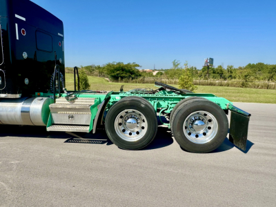 Kenworth W900L truck chassis side view showing green frame and dual rear wheels with aluminum fuel tank and side steps.