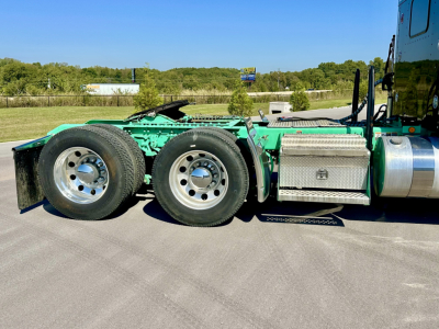 Kenworth W900L truck chassis side view showing rear dual rear axles, green paint, aluminum fuel tank, tool box, and steps.