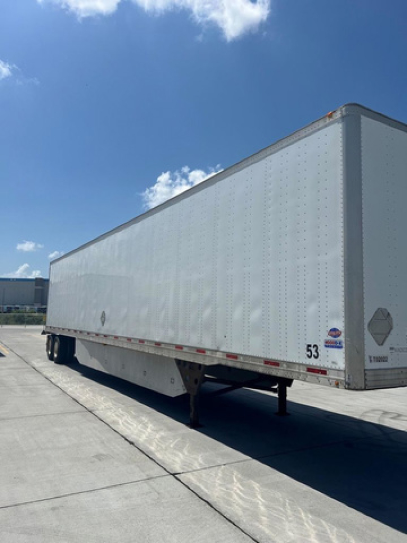 2014 Utility Van trailer showing side of rectangular cargo box on a raised landing gear. Visible text includes plate and sticker markings near the front corner and a small circular logo.