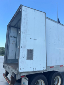 Rear open cargo area of a utility van trailer showing interior doorway and exterior riveted aluminum panels.