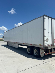Trailer side view showing enclosed box with dual rear doors and wheels undercarriage, utility van trailer. Visible text not legible.
