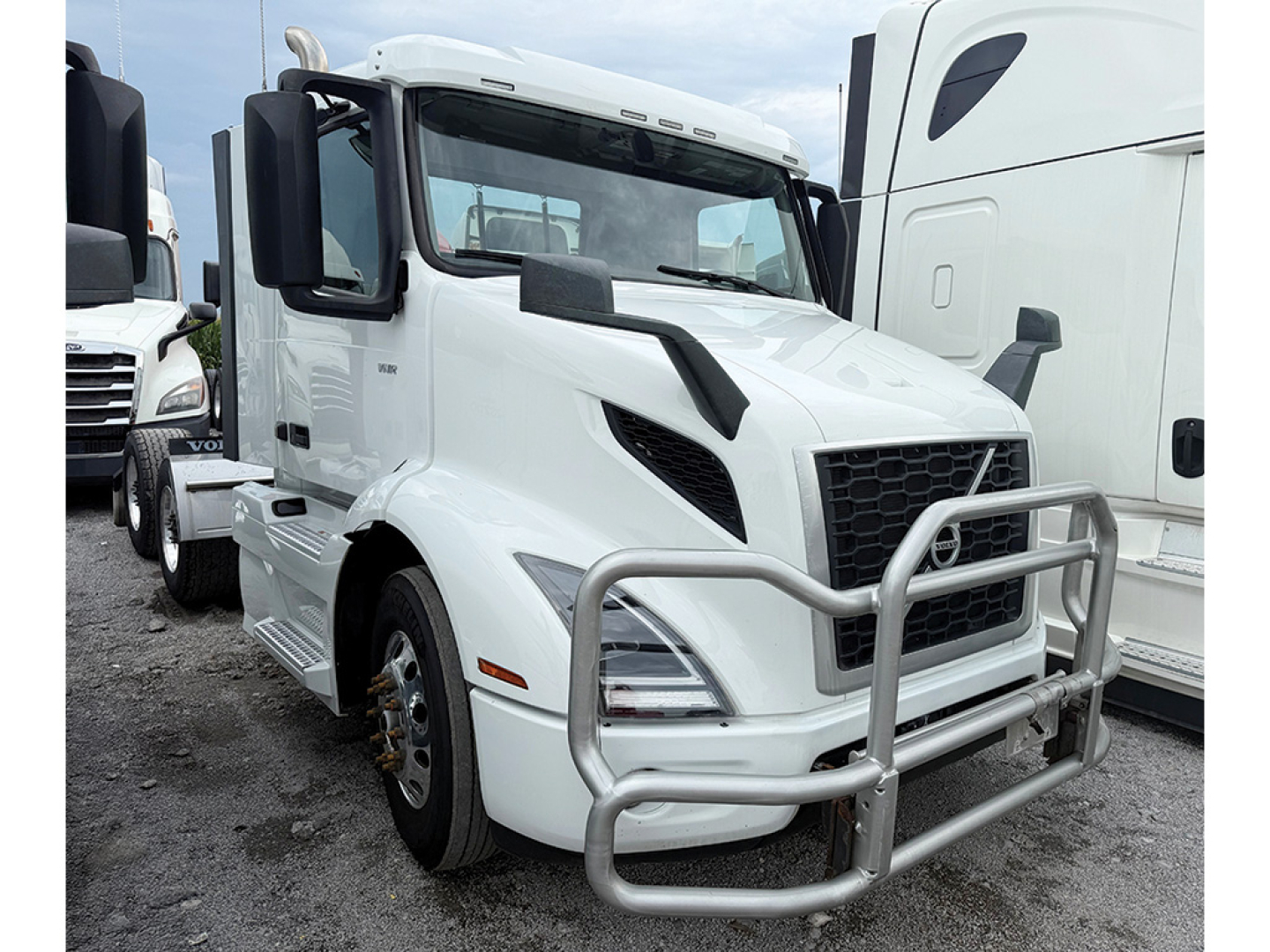 Volvo VNR truck in white with front bull bar and cab mirrors visible, docked among other trucks.