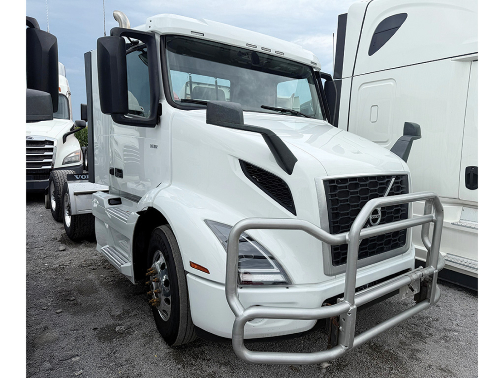 Volvo VNR truck in white with front bull bar and cab mirrors visible, docked among other trucks.