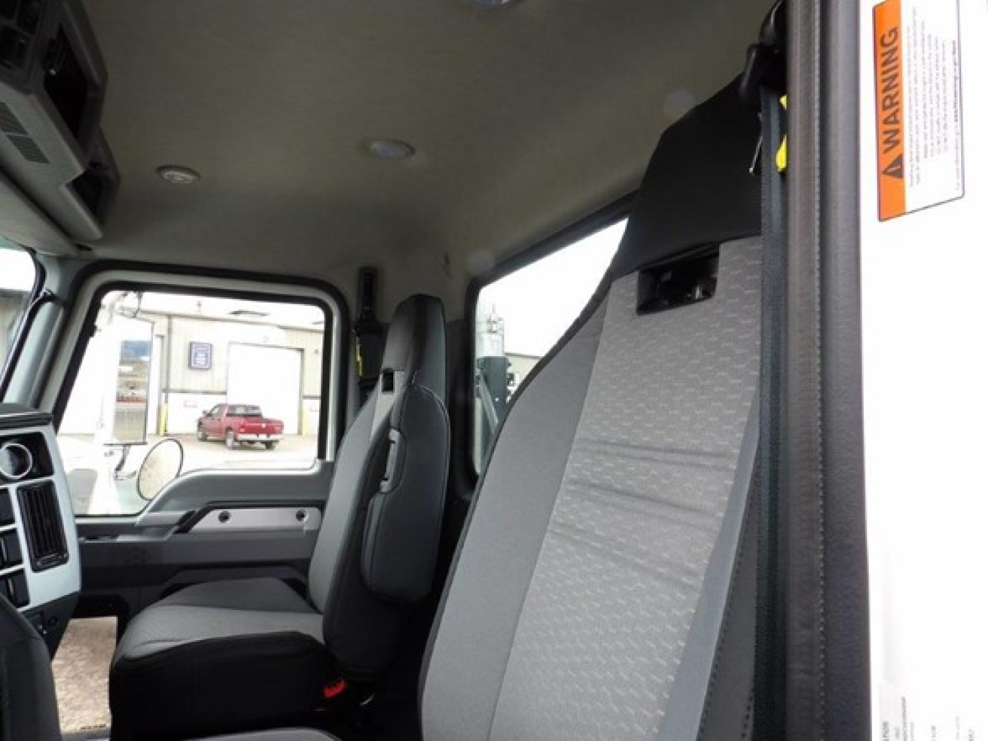 Cab interior of a 2025 Mack GR64B truck showing front seats and partial dashboard; a warning sticker is visible on the door post.