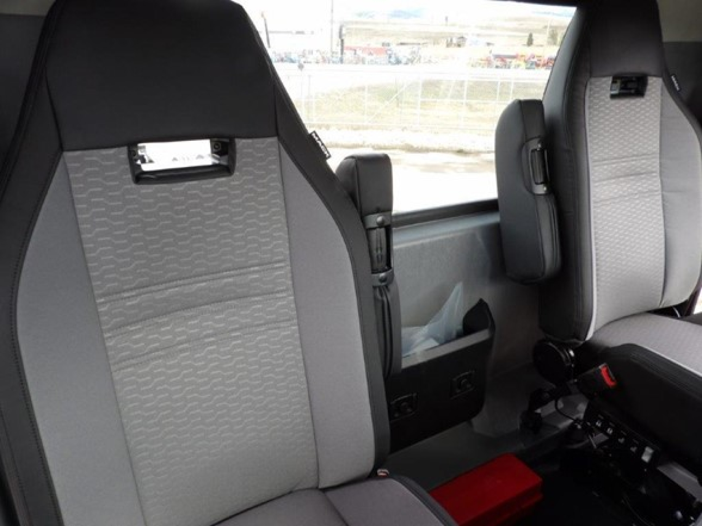 Cab and chassis interior showing gray upholstered seats, window view, and center console area in a new Mack GR64B truck.