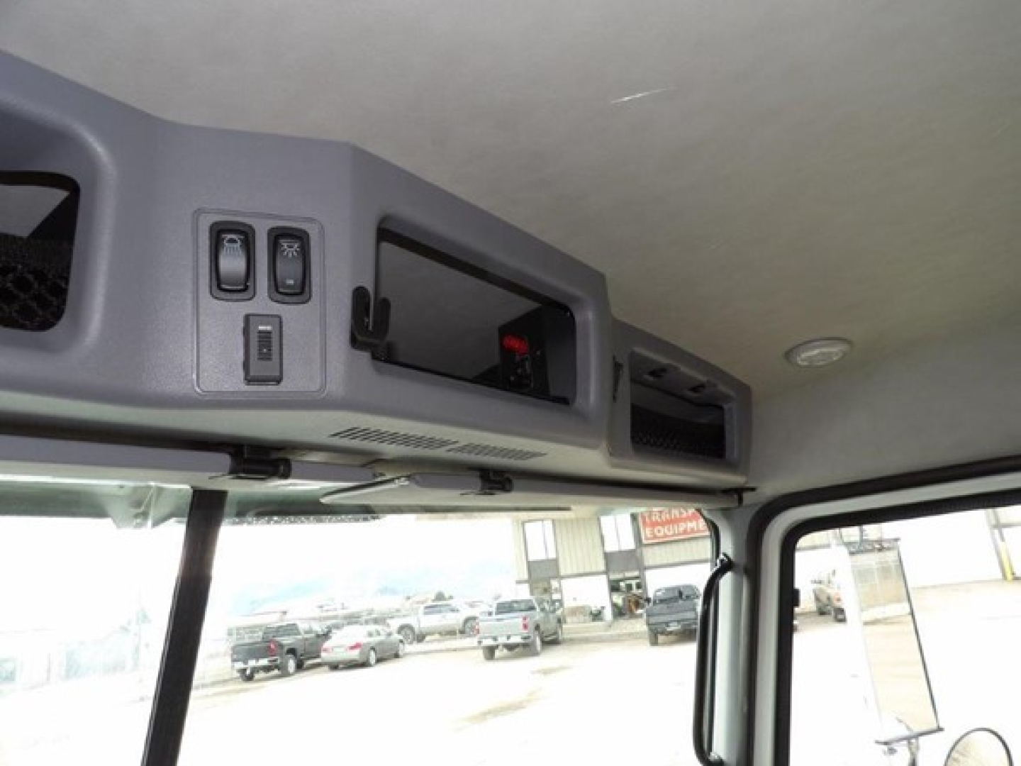 Cab interior roof console with switches and storage panel in a Mack GR64B cabin chassis showing overhead compartments and windows.