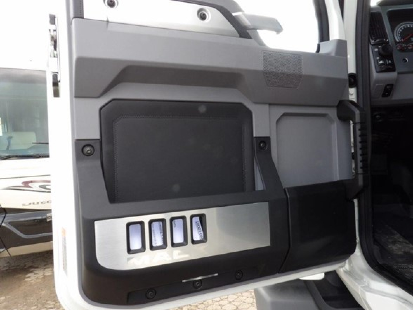 Vehicle door panel of a 2025 Mack GR64B cab and chassis showing control switches and storage panel.