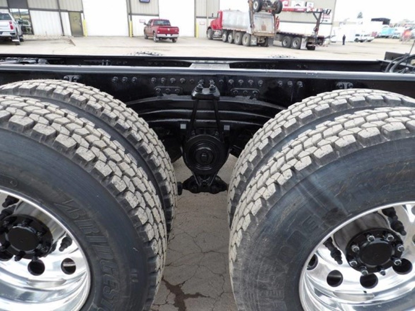 Dual rear axle undercarriage of a 2025 Mack GR64B showing suspension, differential, and large off-road tires with chrome rims.