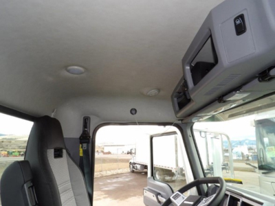 Cab interior of a 2025 Mack GR64B truck showing overhead console, sun visors, and driver's seat with seatbelt. Window view includes another truck outside.