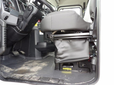 Truck cab interior from driver side showing driver's seat and floor with pedals and dashboard; seat base and cabin area visible.