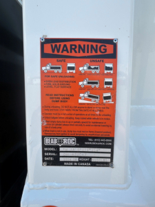 Label plate with WARNING for BEAUROC/??? on dump truck body; pictograms of safe unloading procedures and model/serial/date fields.