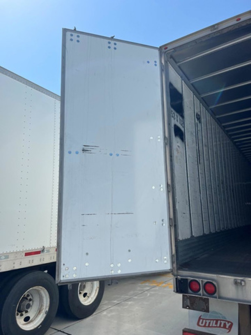 Utility van trailer rear door and open cargo area showing metal interior walls and rear lights.