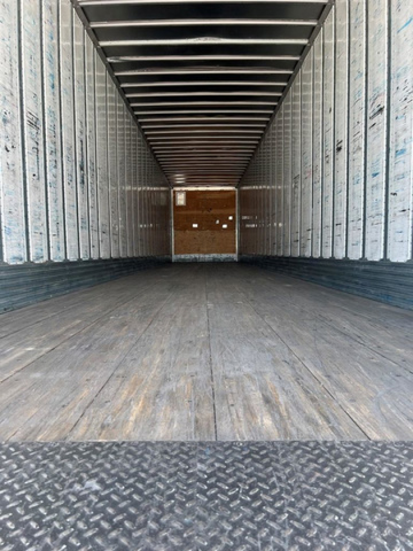 Trailer interior showing empty cargo area with wooden floor, metal side walls, and entry at far end; used utility van trailer.