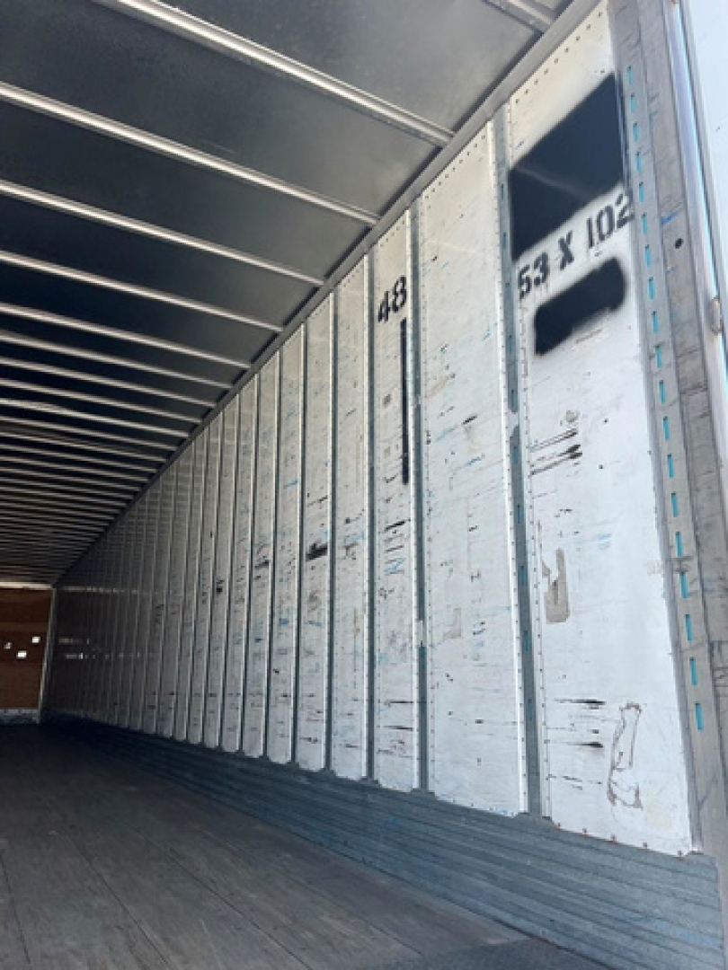 Trailer interior side wall with vertical metal walls, numbers like 149 and 534? 102 visible; aluminum cargo trailer with ribbed floor.