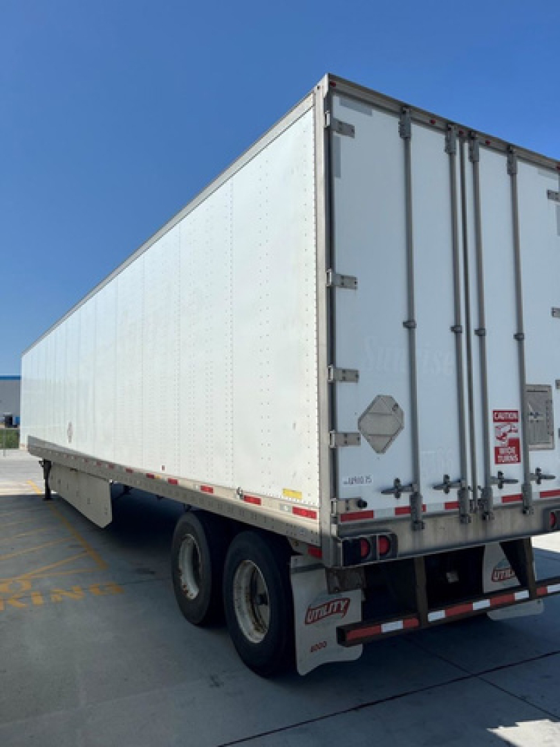 Utility van trailer showing double-axle rear and white refrigerated side panels, rear doors with latches and reflectors.