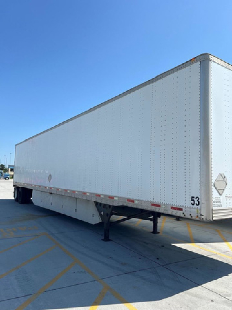 Trailer side view showing white enclosed utility van trailer with support legs and reflective markings.