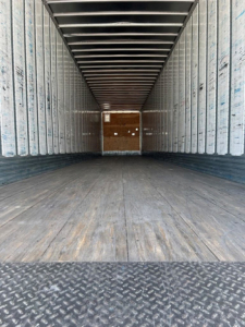 Trailer interior showing empty cargo area with wooden floor, metal side walls, and entry at far end; used utility van trailer.
