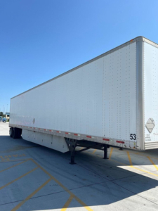 Trailer side view showing white enclosed utility van trailer with support legs and reflective markings.