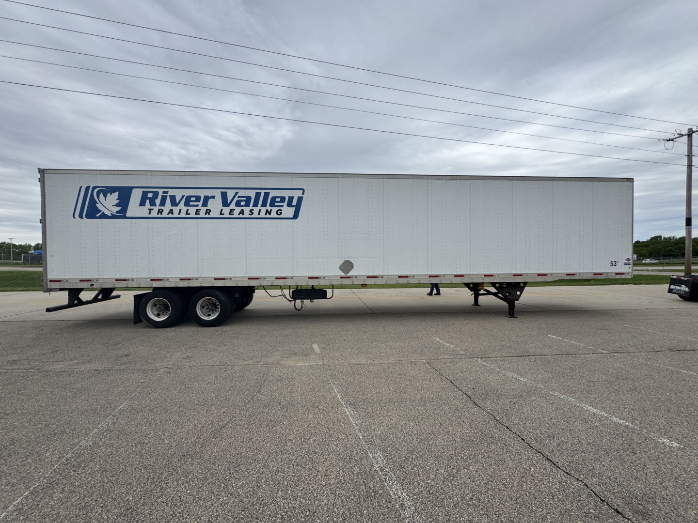 Trailer side view showing River Valley Trailer Leasing logo on a long utility trailer with dual rear axles in a parking lot.