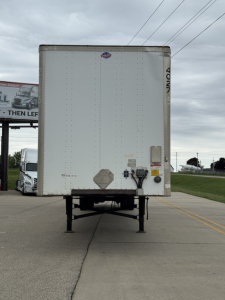 Rear view of a 2014 Utility 4000D-X trailer on a trailer lot. The back doors and undercarriage are visible, with a level surface and a small Diamond Plate spare area, and a name plate near the lower right.