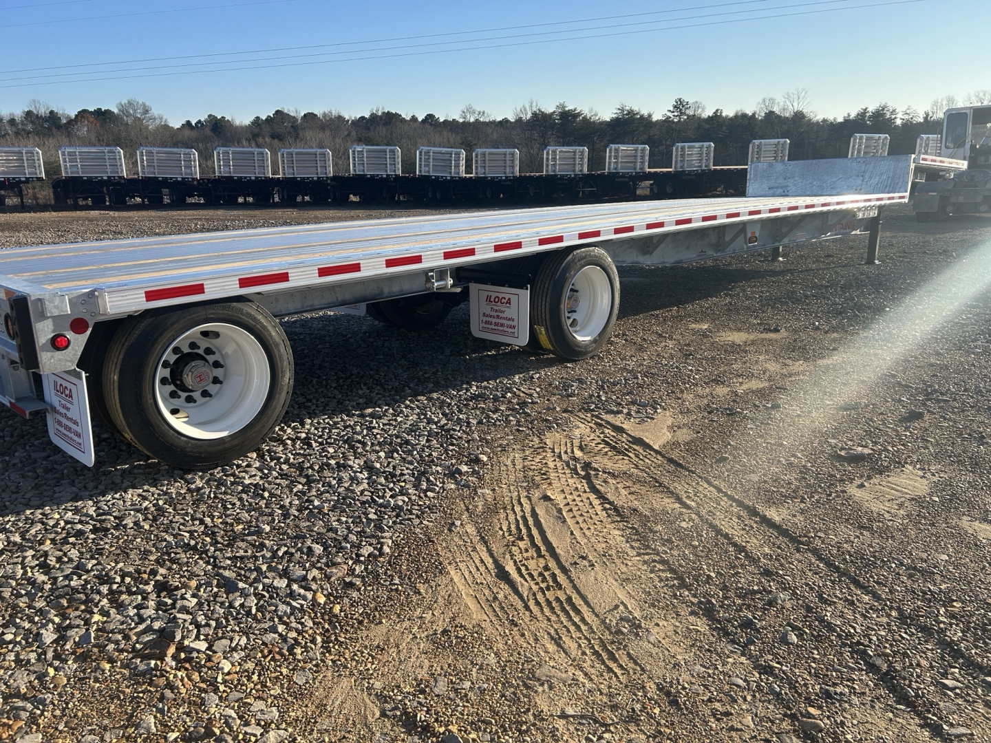Flatbed trailer with galvanized surface and wide spread axle configuration, 48' combo drop deck, side rails and red/white reflective tape.