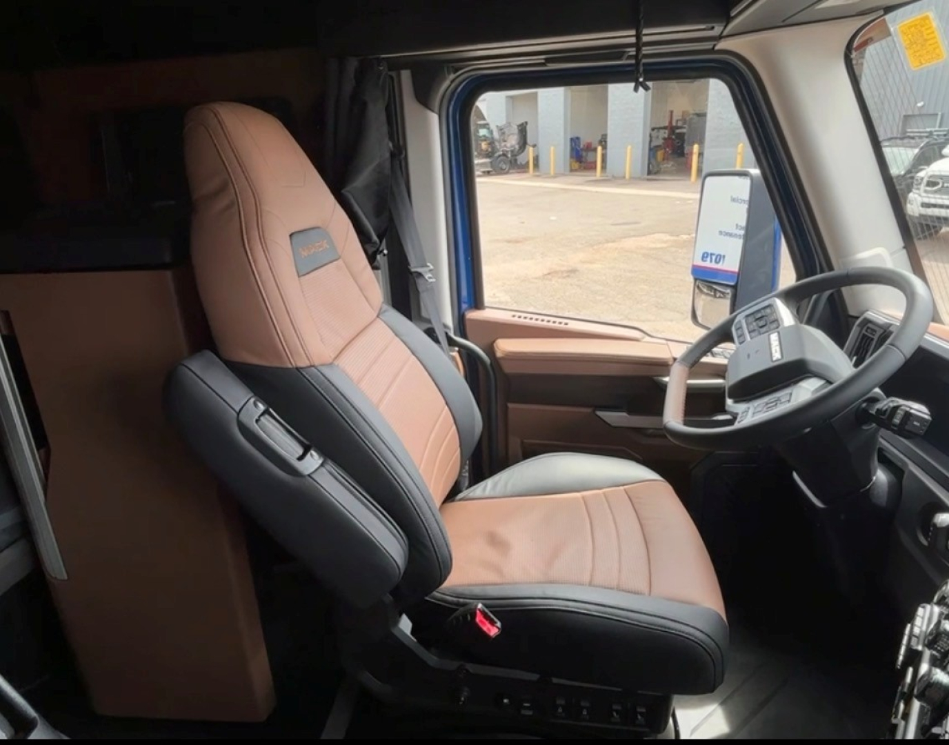 Truck cab interior showing tan and black driver's seat with Mack branding and steering wheel,