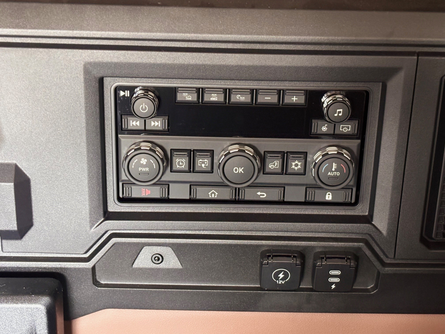 Cab dashboard panel of a Mack PR64T76H truck showing control cluster with buttons, knobs, and display screen.