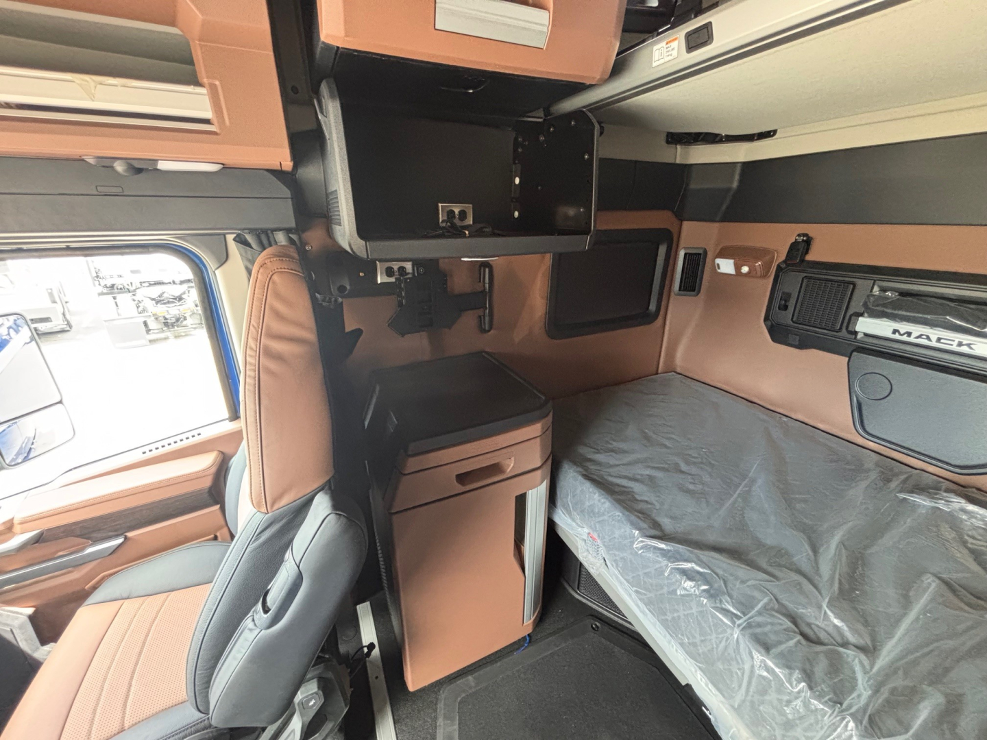 Mack PR64T76H truck cab interior showing sleeper bed with brown and black storage compartments, overhead cabinets, and side paneling.