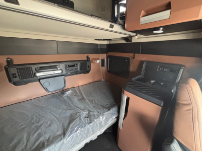 Interior cab of a 2027 Mack PR64T76H sleeper: dashboard panels, storage, and brown leather seats visible in the bunk area.