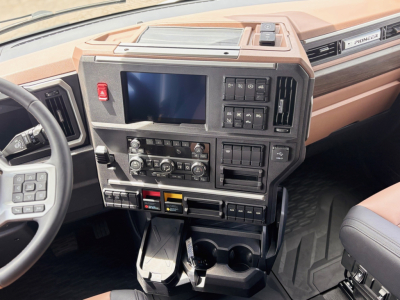 Cab interior of a 2027 Mack PR64T76H showing dashboard with large touchscreen, control panel, cup holders, and storage pockets.