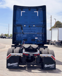 Back view of a blue Mack PR64T76H truck tractor showing rear chassis, dual rear axles, mud flaps with Bruckner's logo, and fifth wheel housing.