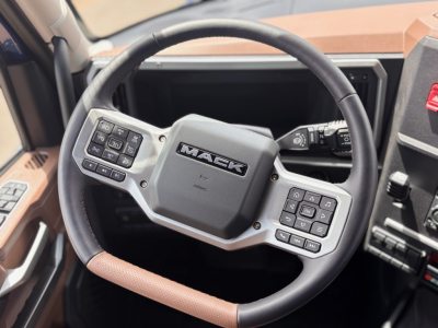 Mack PR64T76H steering wheel and dashboard controls in a new truck cab, center badge reads MACK, left and right control clusters visible.