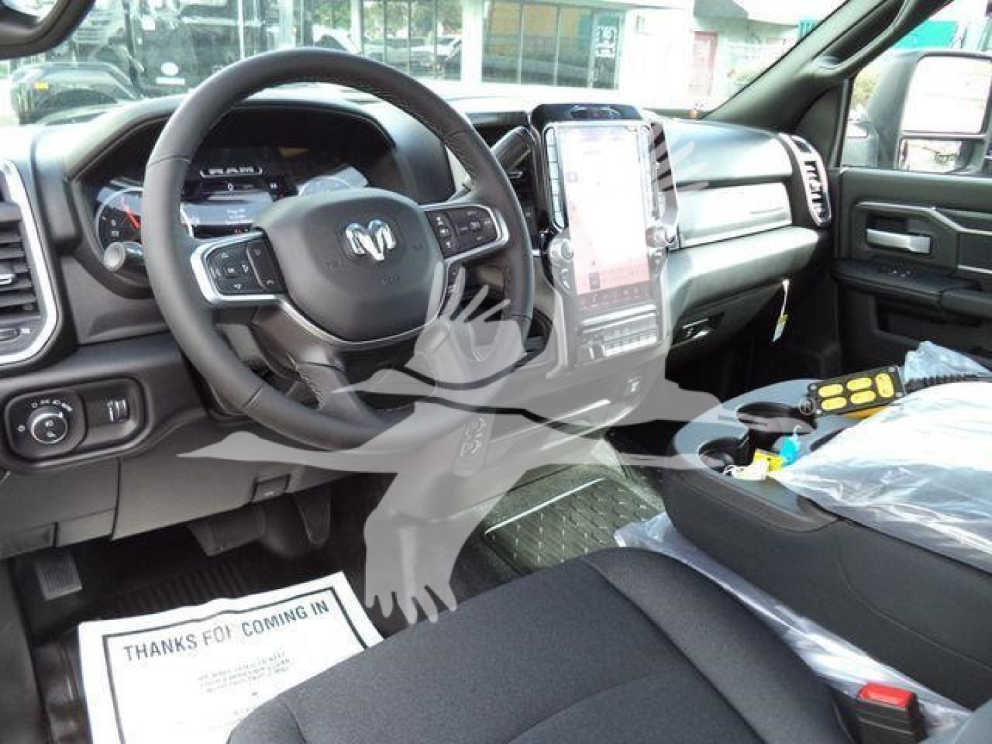 Interior driver’s area of a Ram 4500 truck showing steering wheel, large center touchscreen, and dashboard; visible floor mat and protective plastic on seats.