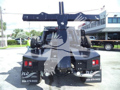 Truck rear view with large hitch/mounted crane/hoist on bed, spare tires on both sides, taillights visible, TLC branding and stock numbers on bumper.