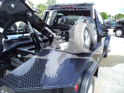 Truck bed with heavy-duty flatbed and mounted winch system, Ram 4500 style chassis, spare tires mounted on cab rear, diamond plate surface, towing equipment visible.