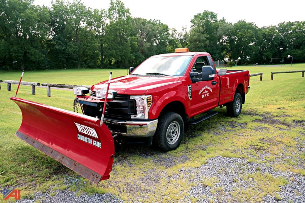 Ford F-350 Super Duty truck with a front plow in a field, red body, single rear wheel, utility branding on door.