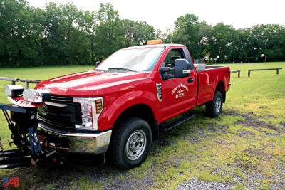 Red Ford F-350 Super Duty pickup with service decals and plow attachment, side view in grassy lot.